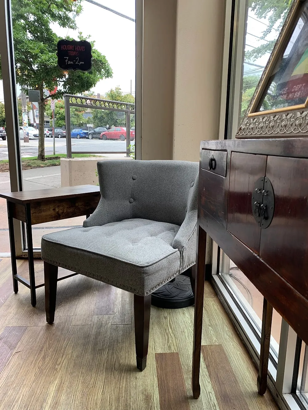 A gray buttoned armchair by the front window, with the street and a small chalkboard beyond.