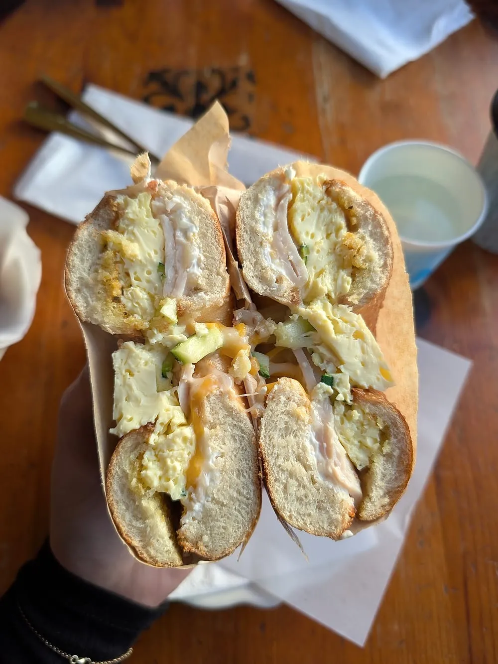 Breakfast bagel sandwich with egg, zucchini and cream cheese, cut in half on brown paper.