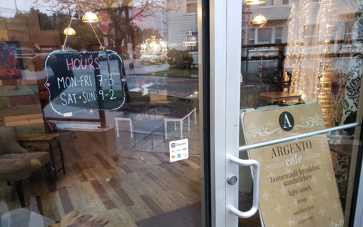 The front door of Cafe Argento with the hours chalkboard reading Mon–Fri 7–3, Sat and Sun 9–2, and the sandwich board inside.