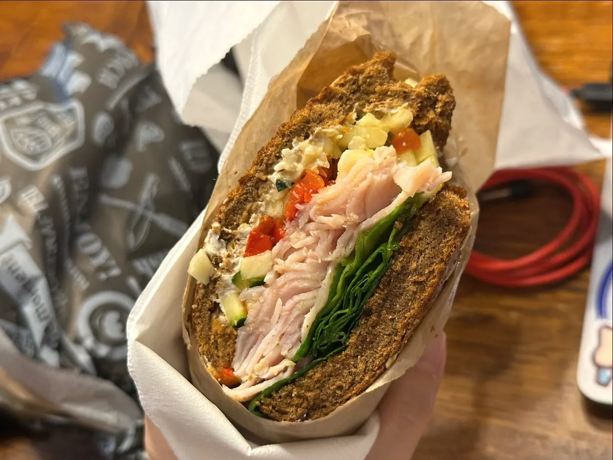 Turkey lunch sandwich on a dark seeded bagel with spinach and roasted red pepper.